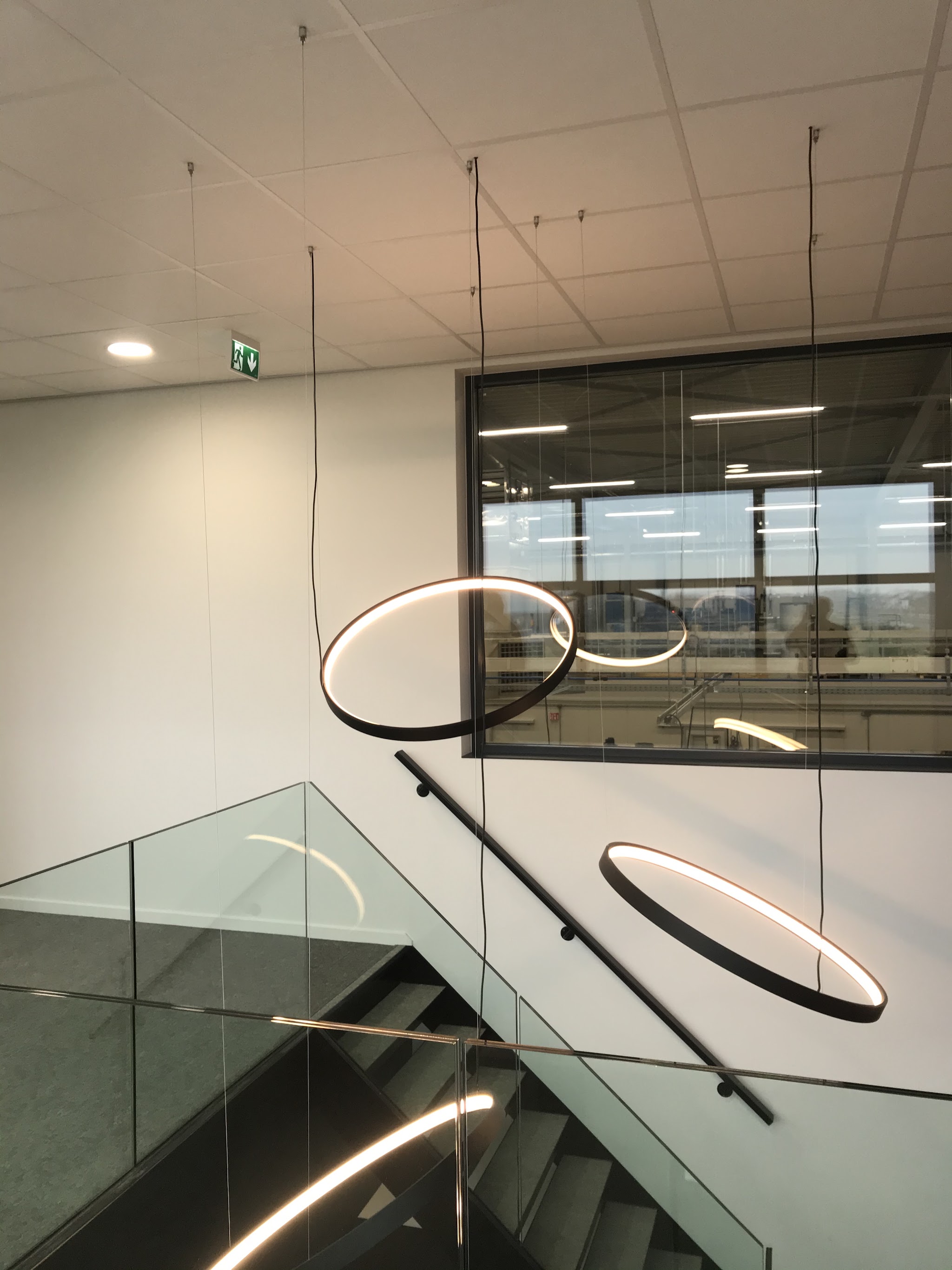 Ringvormige hanglampen boven een trap met glazen balustrade in een kantoor